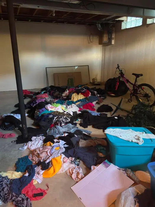A basement floor covered in clothes, boxes and bins