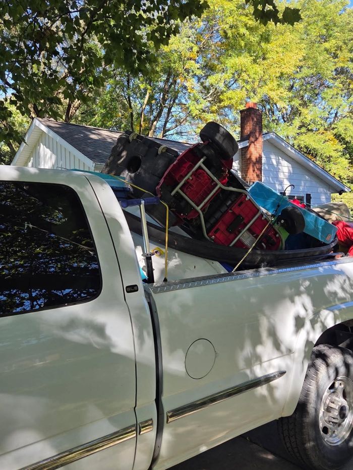 A white Chevy pickup truck with its bed loaded high with junk, including red and blue plastic toys, strapped down